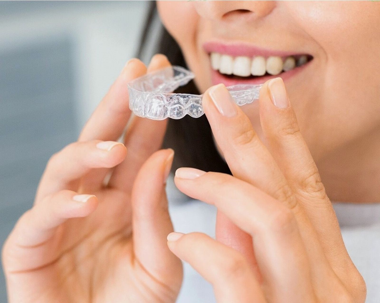 A woman holding a transparent clear aligner tray up between her fingertips